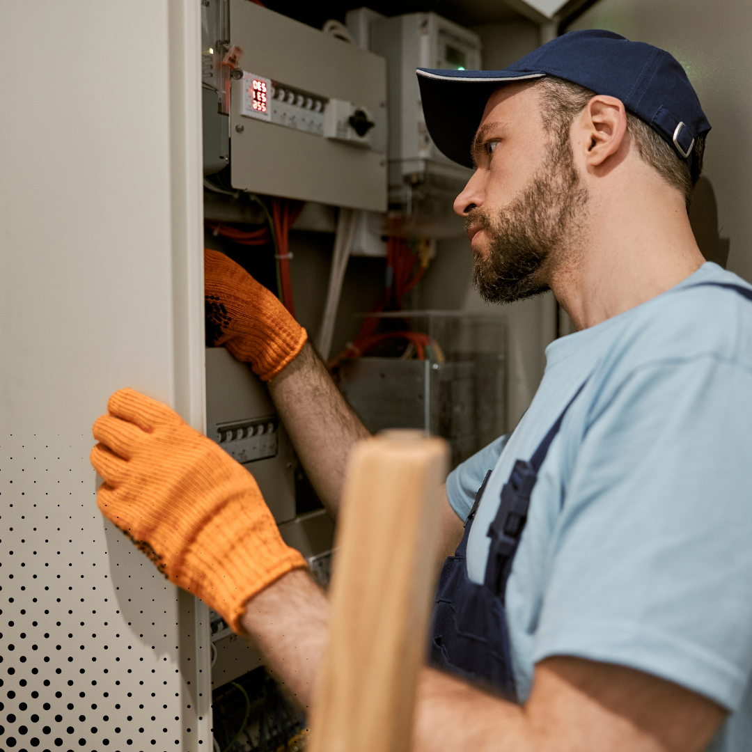 The home inspector, dressed in a blue cap and orange gloves, ensures the electrical panel is in proper working order. 