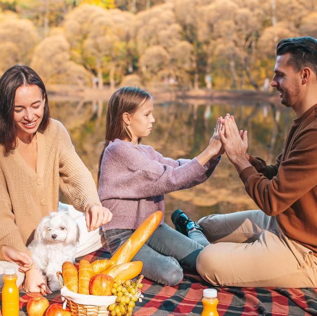 Family enjoying an outdoor picnic by the lake with their dog