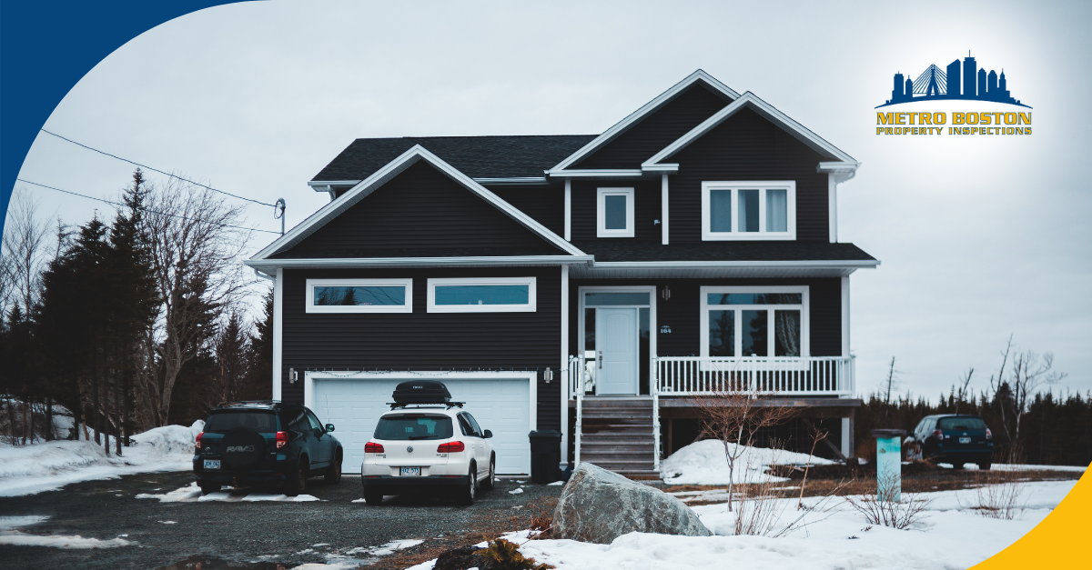 A modern black two-story house with a snowy landscape and cars parked in the driveway