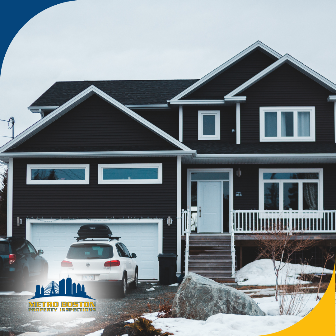 A modern black two-story house with a snowy landscape and cars parked in the driveway