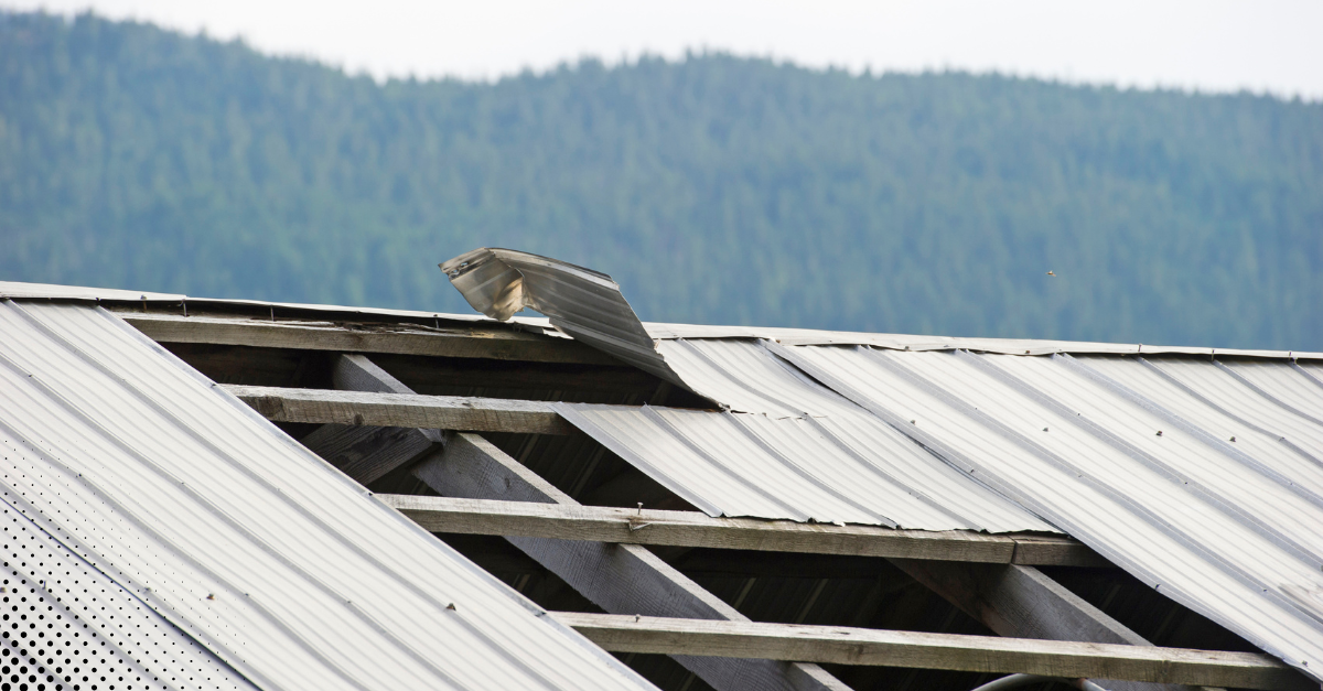 Tornado damage to metal roof with bent panels and exposed beams.