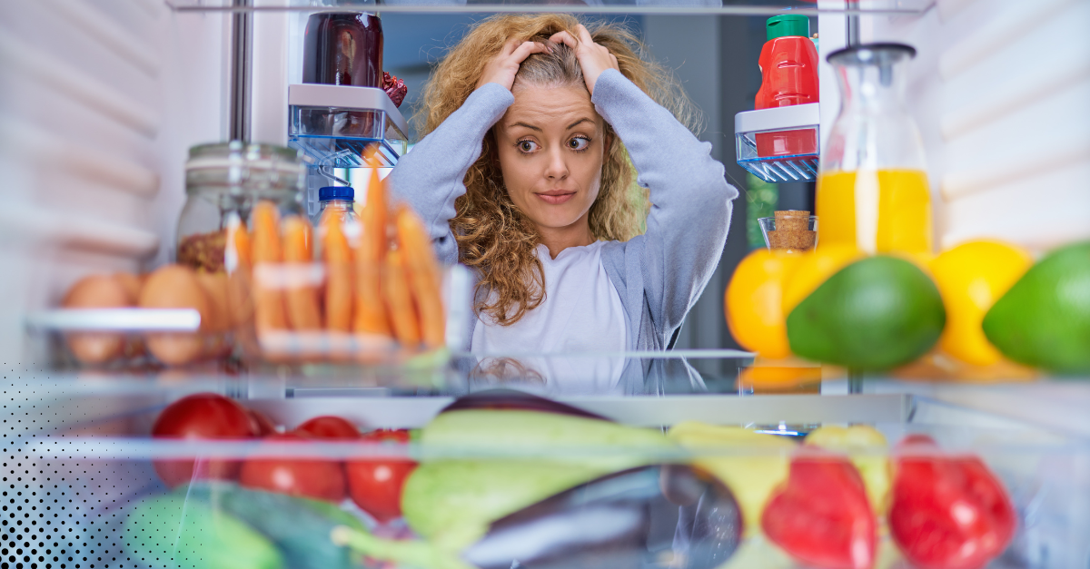 Woman looking stressed while staring into a fridge full of food.